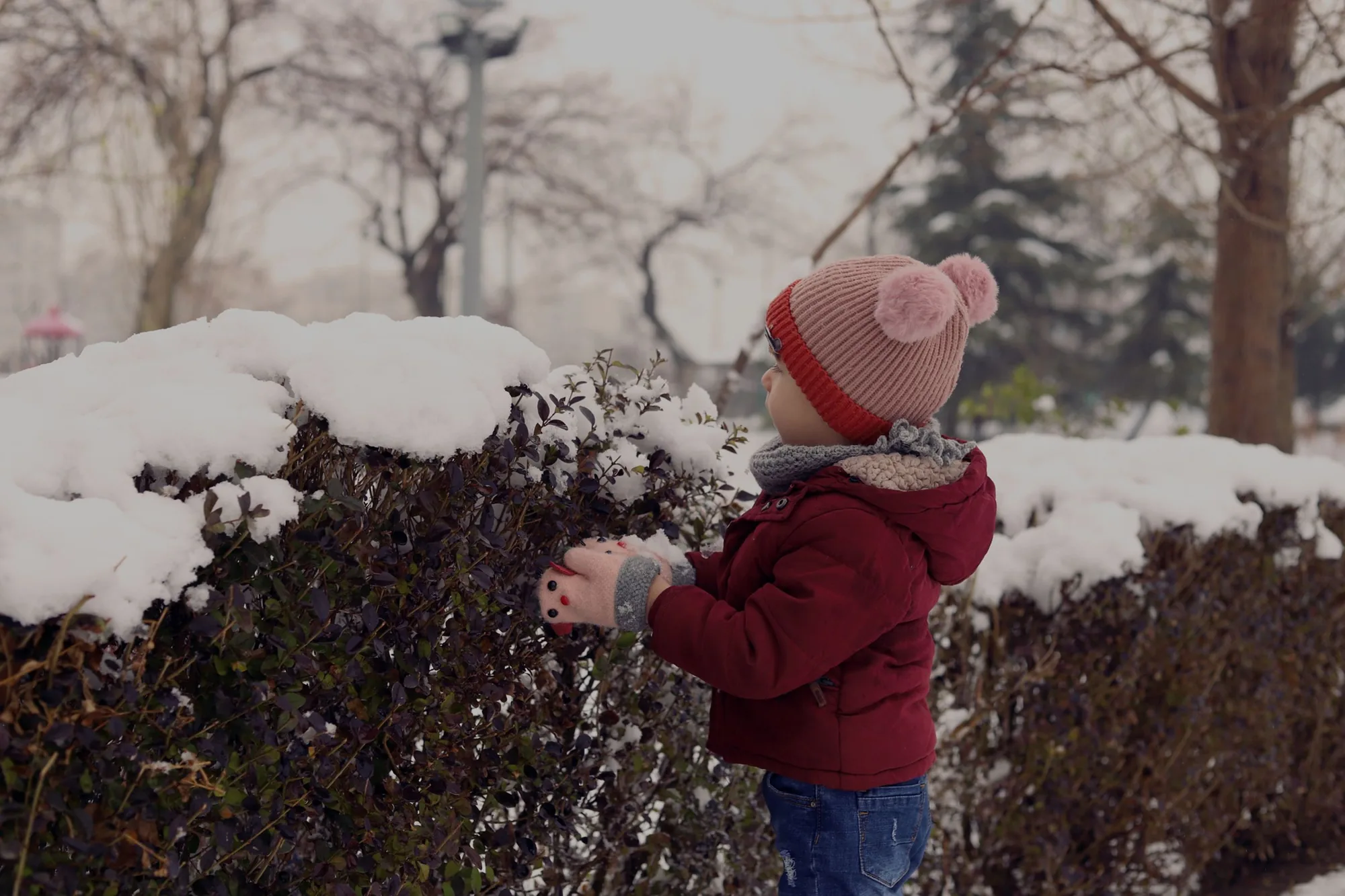 A child in a warm red coat exploring a snow-covered park